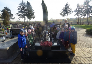Grupa dzieci stoi wokół grobu księdza Bogusława Palenickiego oraz księdza Ryszarda Kolibskiego, w tle inne groby.